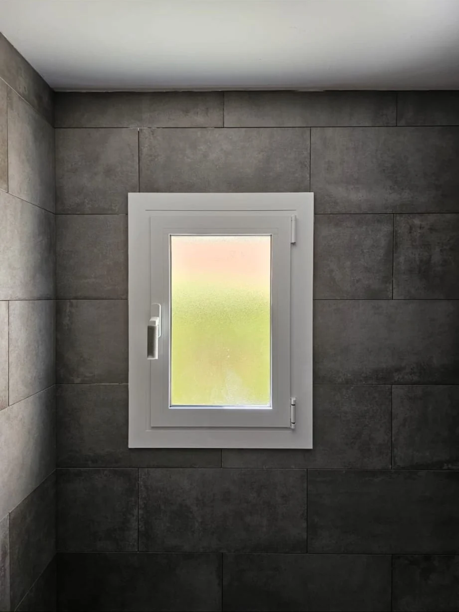 Ventana blanca instalada en baño con azulejo oscuro